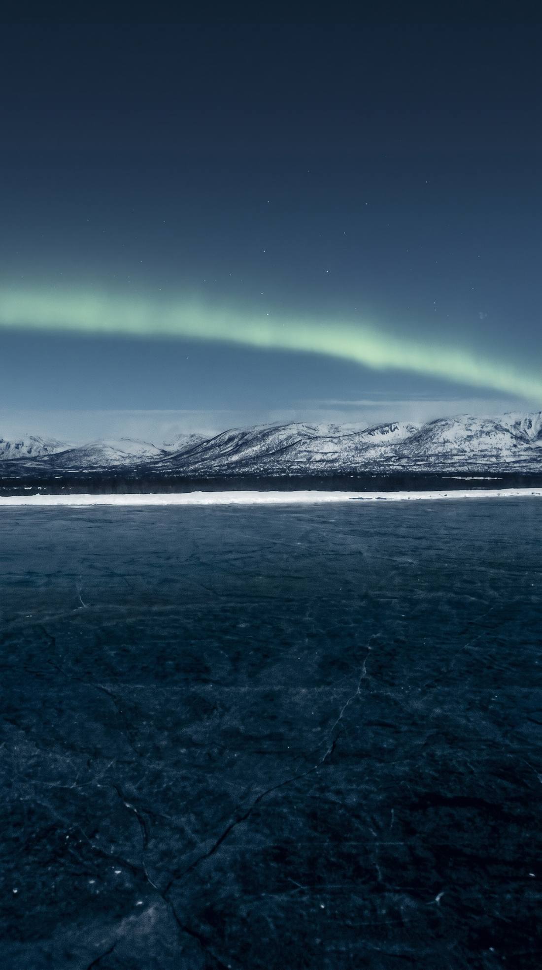 Green aurora over snow mountains and a frozen lake at night.